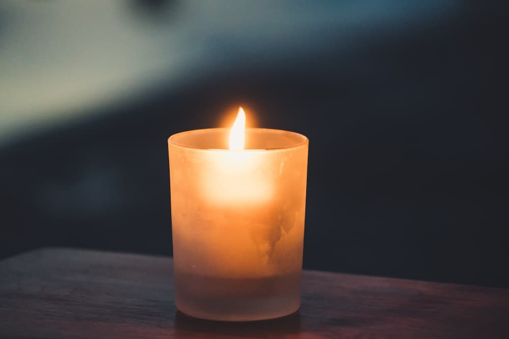 A lit candle glowing in a frosted glass holder