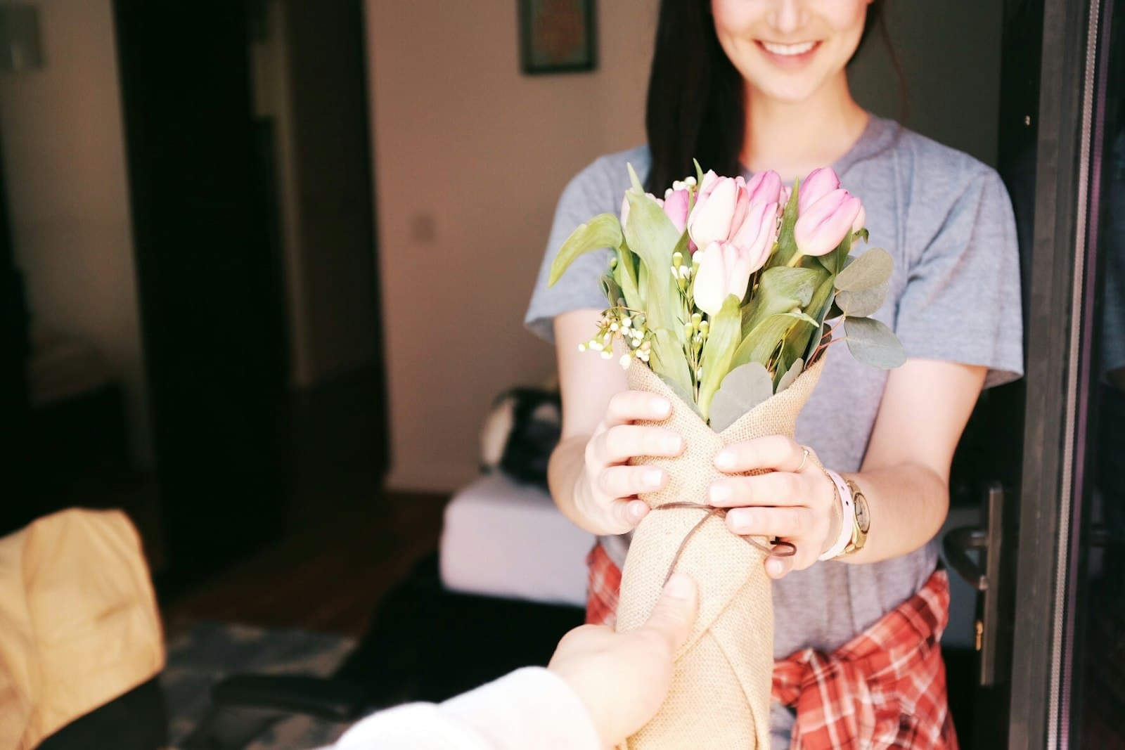 Someone handing a bouquet of pink tulips to a friend